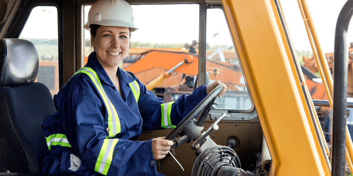 Smiling woman driving construction vehicle.