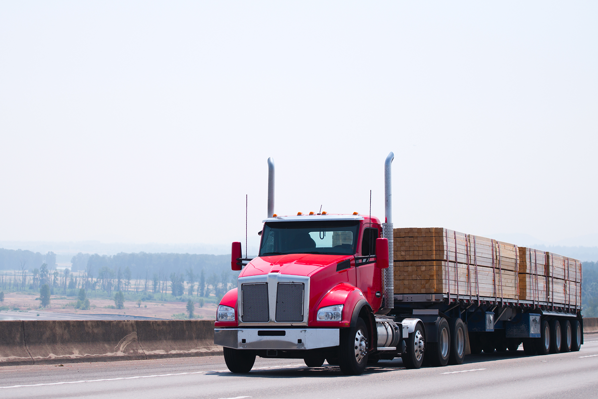 Red truck transporting lumber on highway.