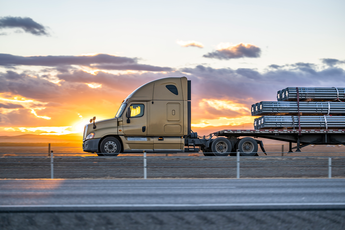 Truck hauling cargo at sunset on highway.